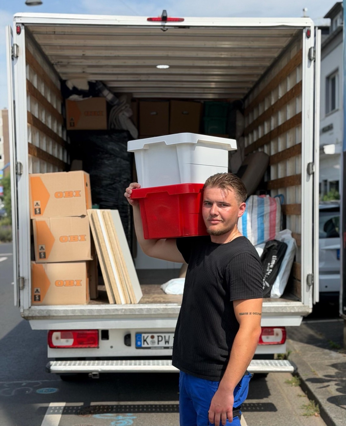 Umzugshelfer trägt zwei Boxen vor dem beladenen Wagen